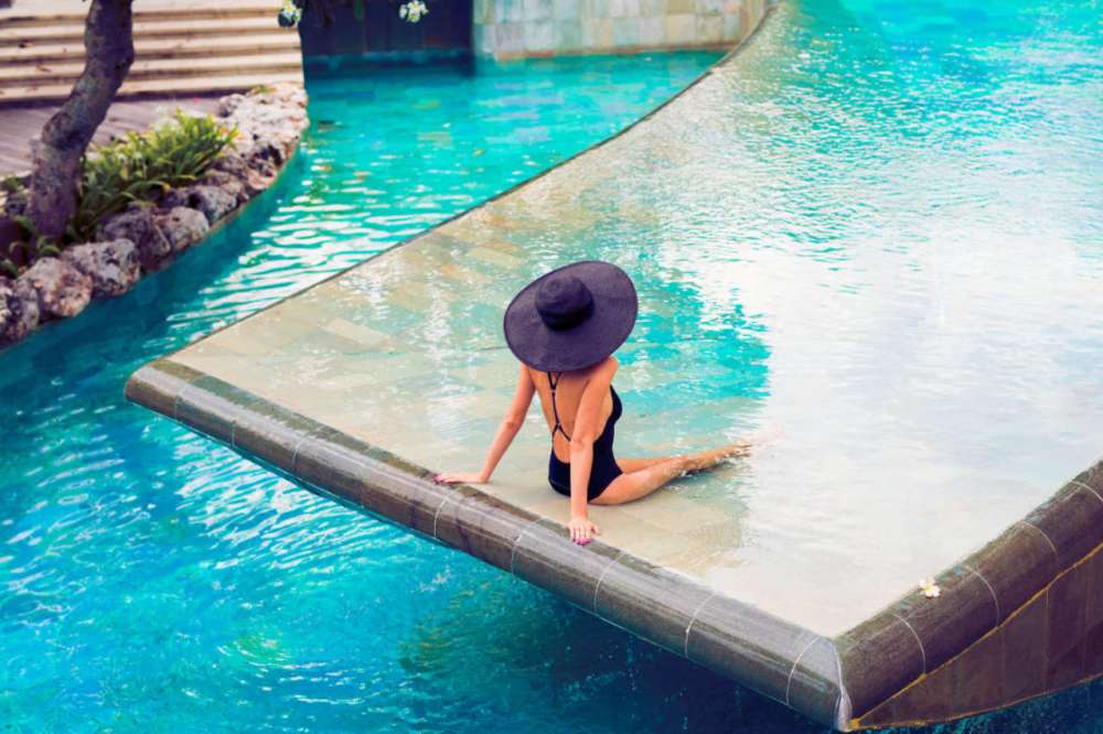 A woman with a large hat sits in hotel's pool.
