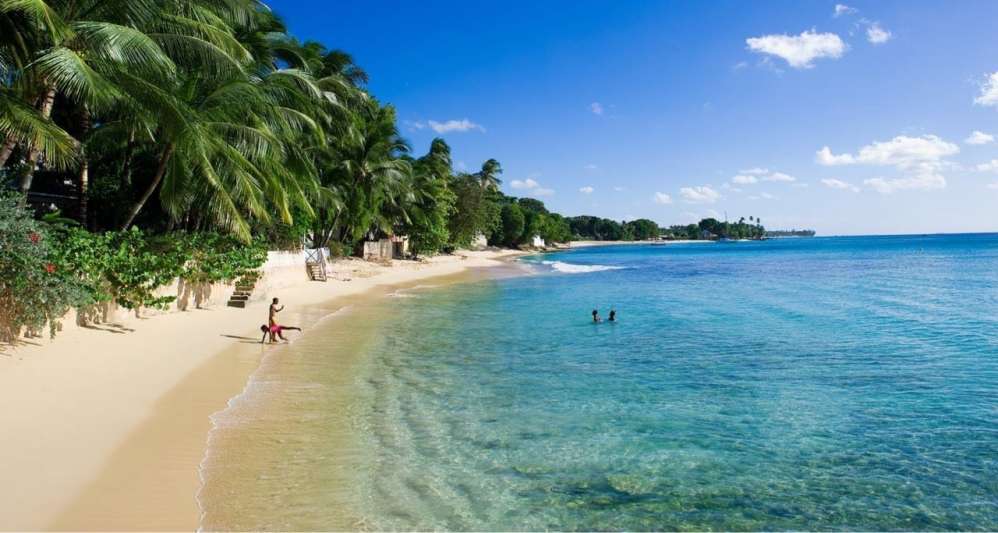 A beach in Barbados with 4 people playing in the sea.